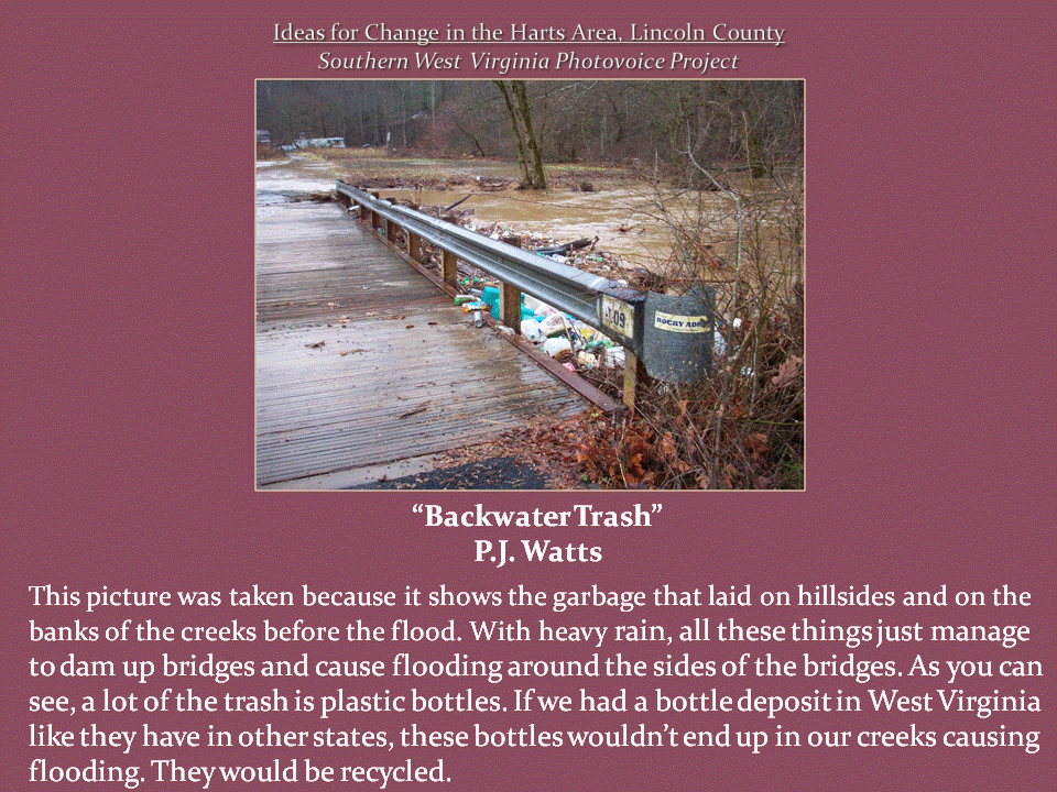 Plastic bottles and other flood debris pile against a bridge guardrail as muddy creek water rises alongside the roadway.