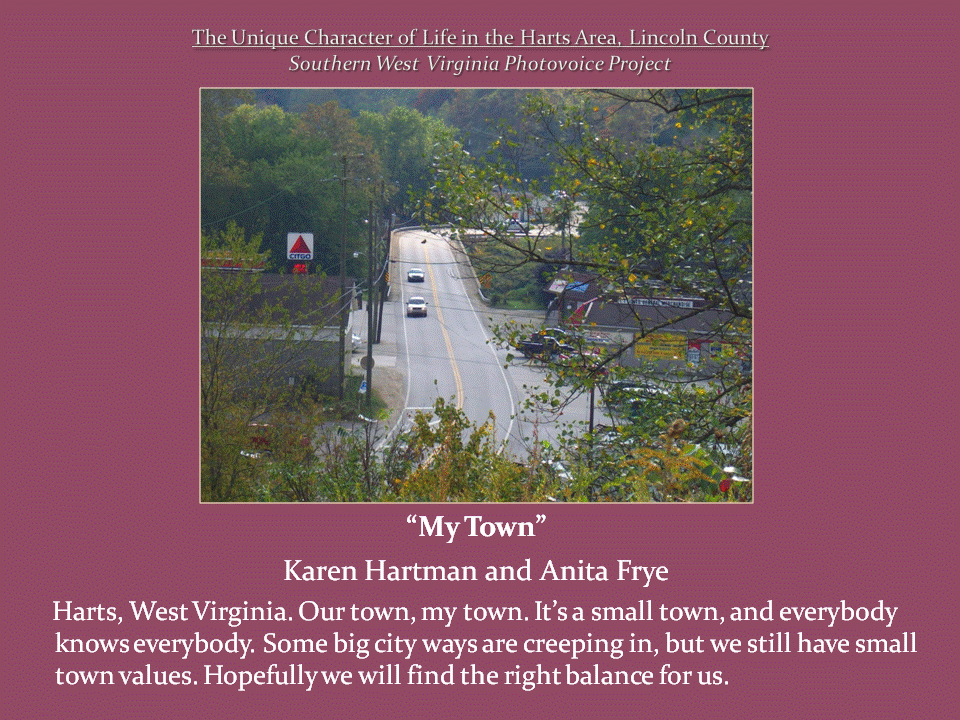 An elevated view of a two-lane road with several cars, a gas station, and buildings surrounded by wooded hills.
