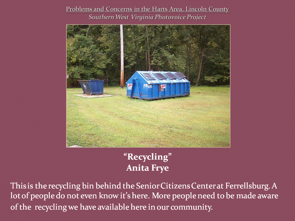 Two large blue waste and recycling containers sit in a grassy clearing surrounded by trees.