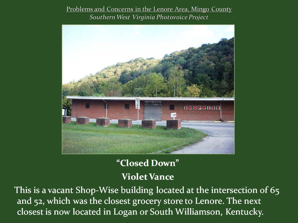 A vacant brick Shop-Wise grocery store with a closed entrance, empty parking area, and wooded hillside behind it.