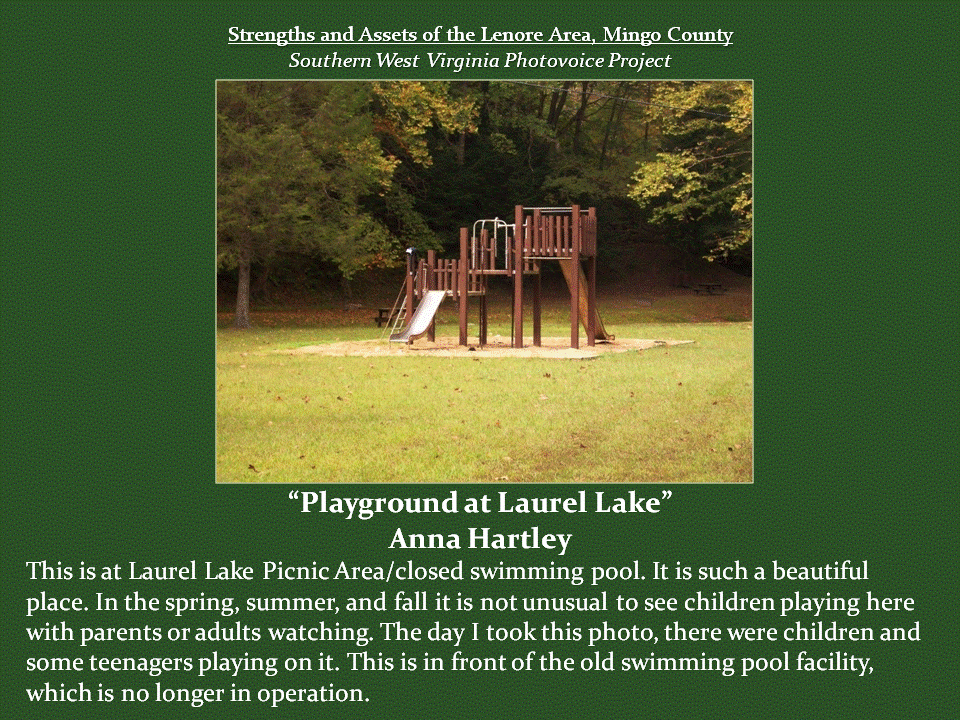 A wooden playground structure with elevated platforms, ladders, and a slide stands in a grassy clearing surrounded by trees at the Laurel Lake Picnic Area. Located near a former swimming pool facility, the playground provides a recreational space where children and families can gather and enjoy the outdoors.