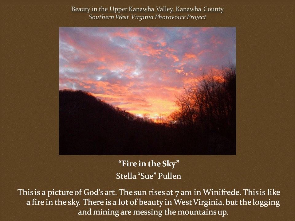 Brilliant orange and pink sunrise clouds spread across the sky above dark mountain ridges and silhouettes of leafless trees.