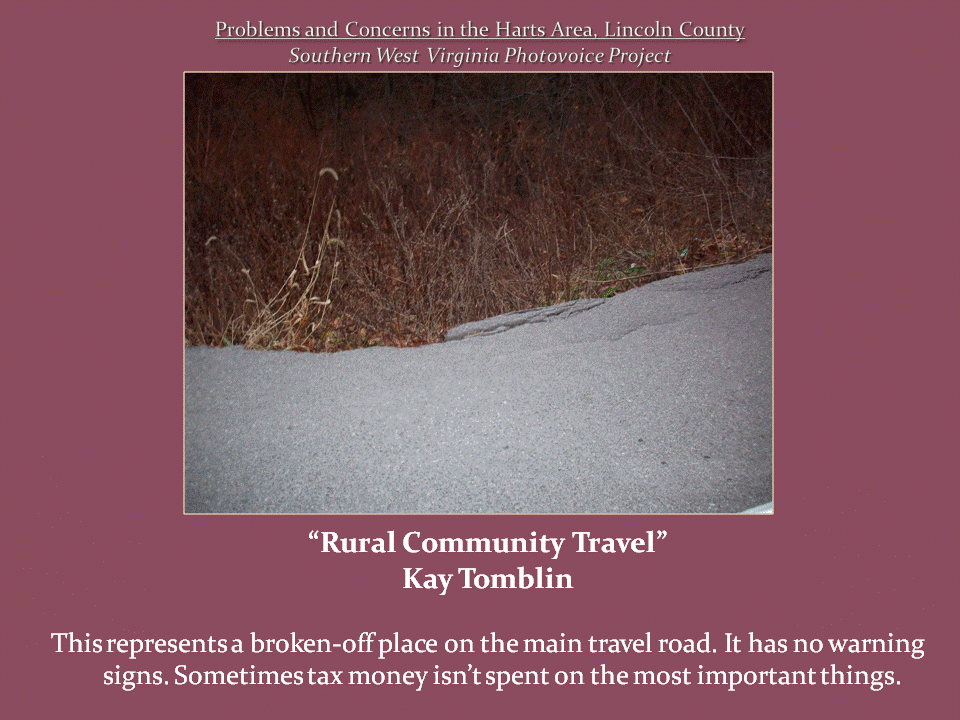 A damaged section of asphalt along the edge of a rural road, with a steep, overgrown embankment below.